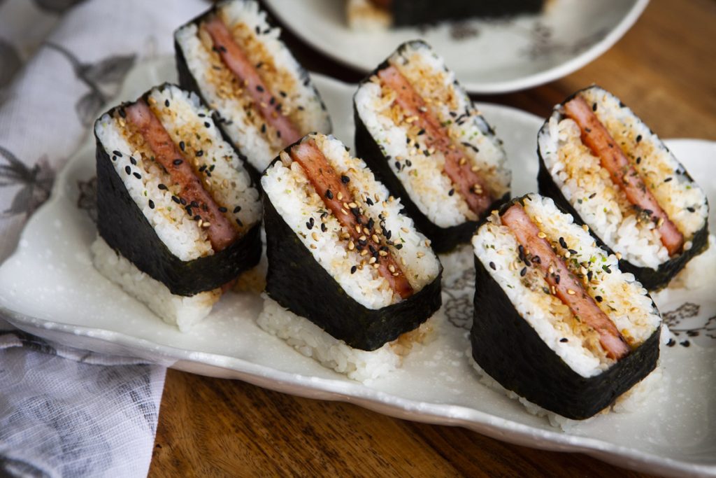 Three musubis cut in half diagonally on a white plate.